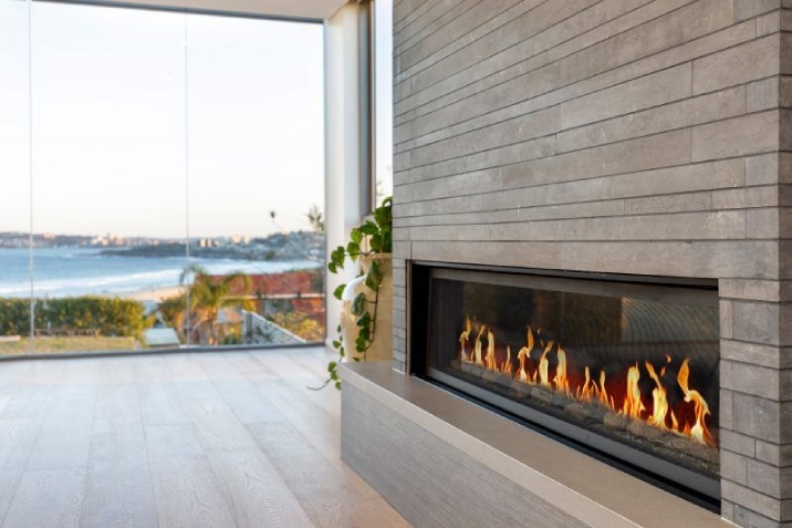 A beautiful indoor fireplace built into a grey timber wall overlooking the ocean.