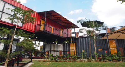 Red and black shipping container homes surrounded by a garden.