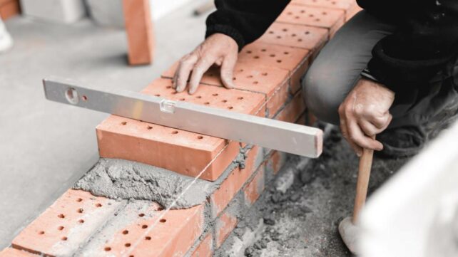 a handyman balancing a level on top of a brick layer