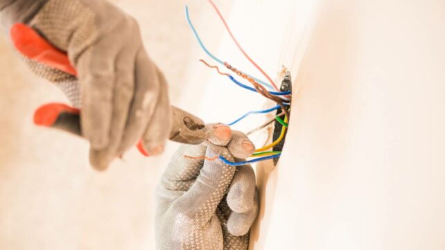 man in glovers using pliers working with electrical wires