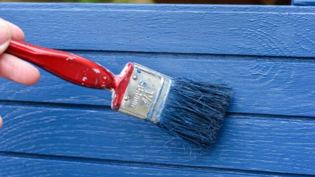 using a paintbrush to paint a wooden surface blue