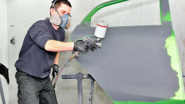 Professional car painter meticulously applying green paint to a car door in an auto body shop. - car respraying cost