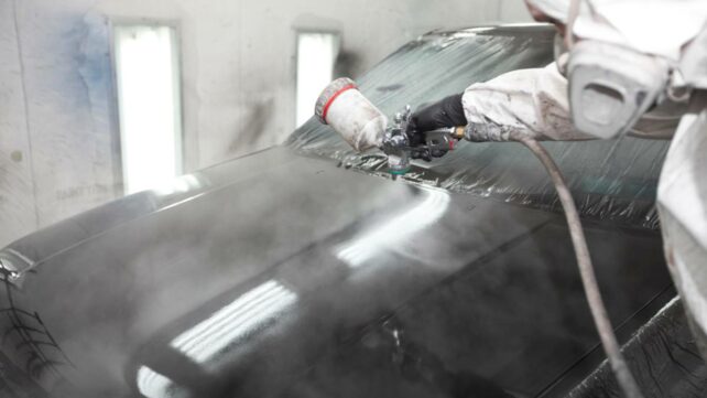 Professional auto painter applying a fresh coat of vibrant blue paint to a car in a workshop. - car respraying cost