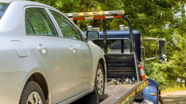 A silver car being towed on a flatbed tow truck - car towing cost