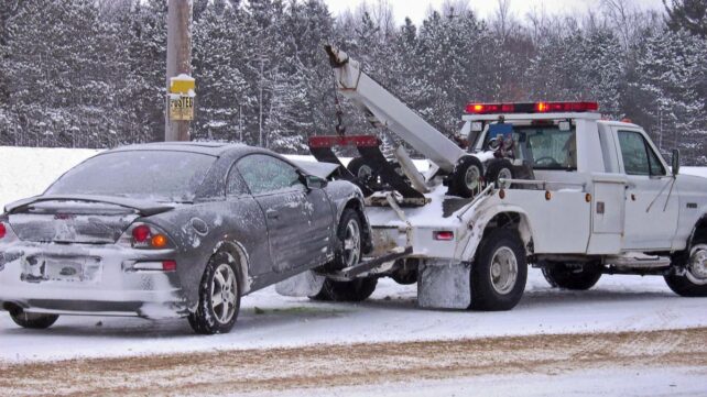 A snowy winter scene with a tow truck and a damaged car - car towing cost