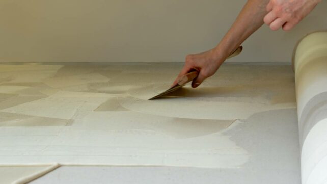 A carpet installer applies glue to the floor in preparation for laying a new carpet in an apartment. - carpet installation cost