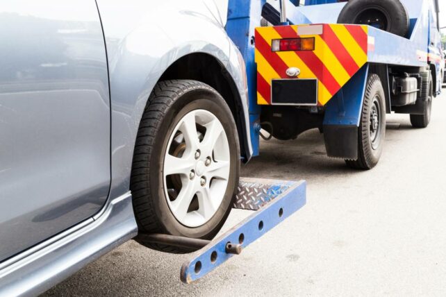 A blue tow truck towing a silver car on a flatbed - car towing cost