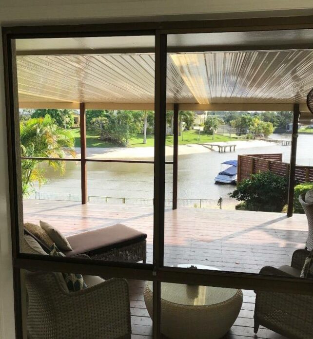 A clean glass window overlooking a serene outdoor deck with seating, a lush green landscape, and a calm waterfront view. - window cleaning cost