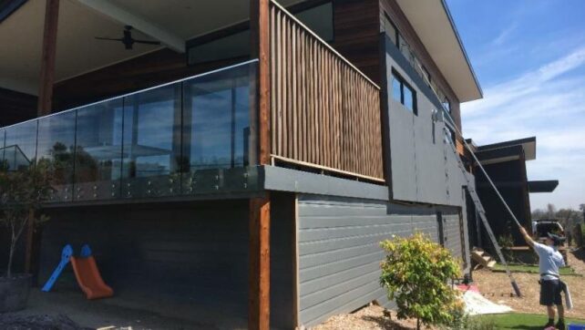 A professional cleaner uses a long pole to clean the upper windows of a two-storey home. - window cleaning cost