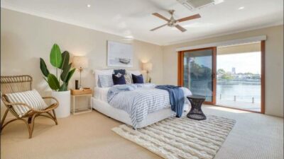 A modern bedroom with neutral tones, featuring a large bed with striped bedding, a cosy armchair, and a scenic window view - housecleaning cost